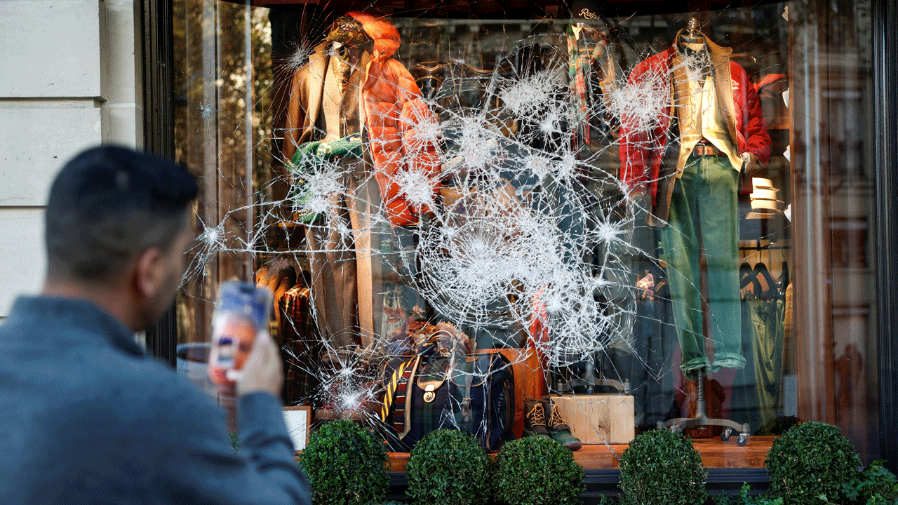 Home 2 A person photographs a shattered clothing store display window in France.