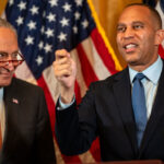 Hakeem Jeffries speaks at a podium with his fist raised to address affordability, as Chuck Schumer stands beside him in front of American flags.
