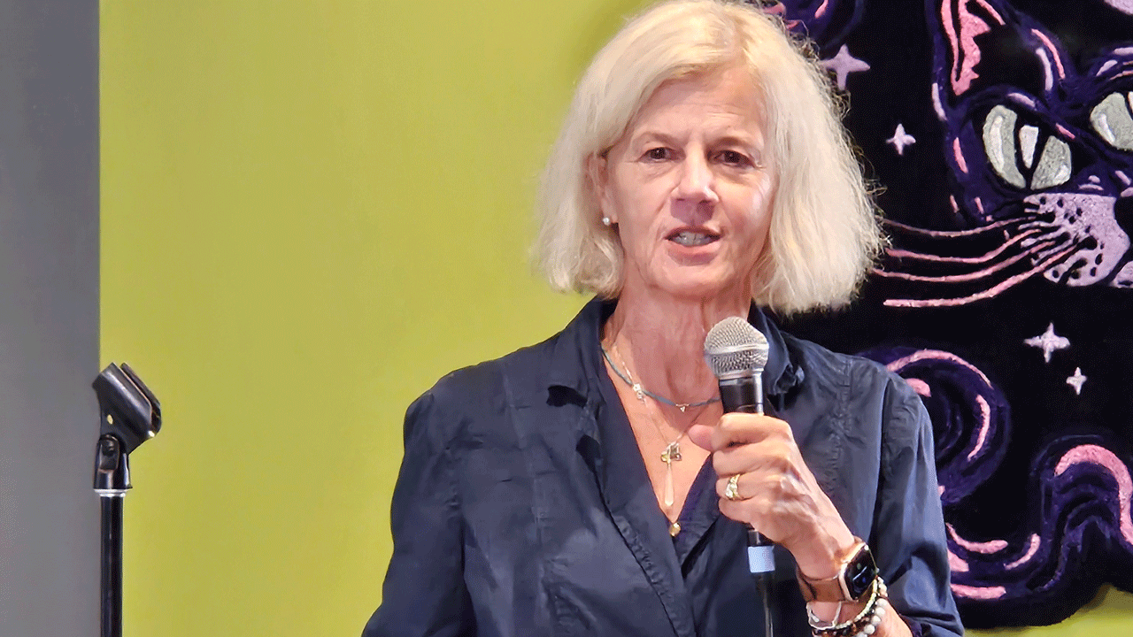 Home 2 A woman with blonde hair speaking into a handheld microphone.