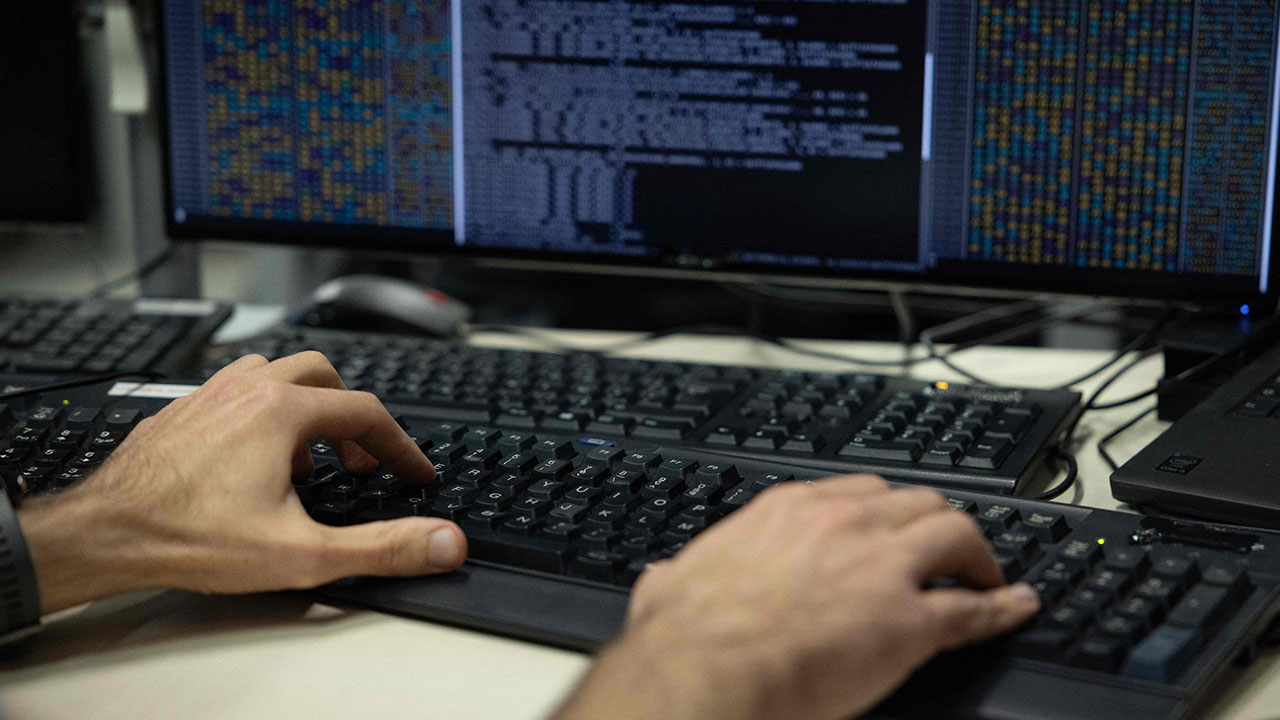 A North Korea IT worker typing on a computer keyboard in front of a monitor displaying lines of code.