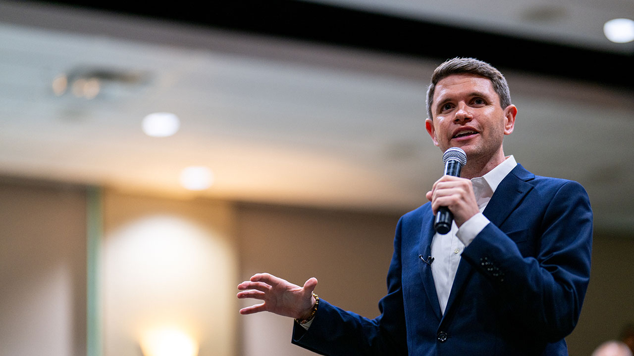 James Talarico speaks to an audience while holding a microphone in a suit jacket.