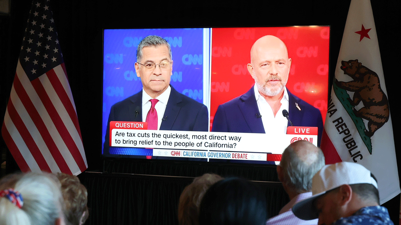A CNN California Governor Debate is shown on a screen between US and California flags, with a text overlay asking, Are tax cuts the quickest, most direct way to bring relief to the people of California, with Hilton and Becerra facing off.
