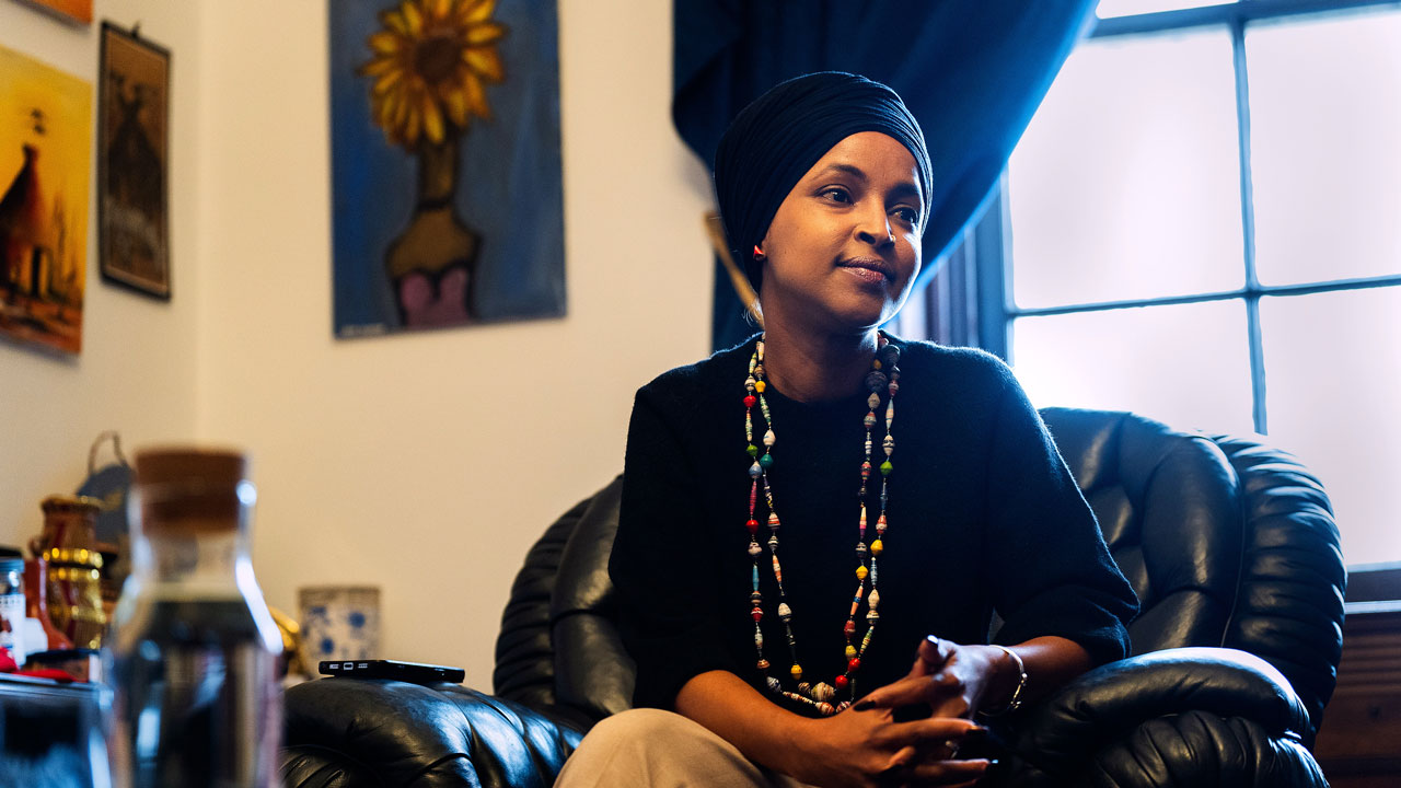 Ilhan Omar wearing a black headscarf and a beaded necklace, sitting in a leather chair.