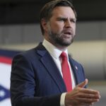 J.D. Vance speaking at a podium in front of an Ohio state flag.