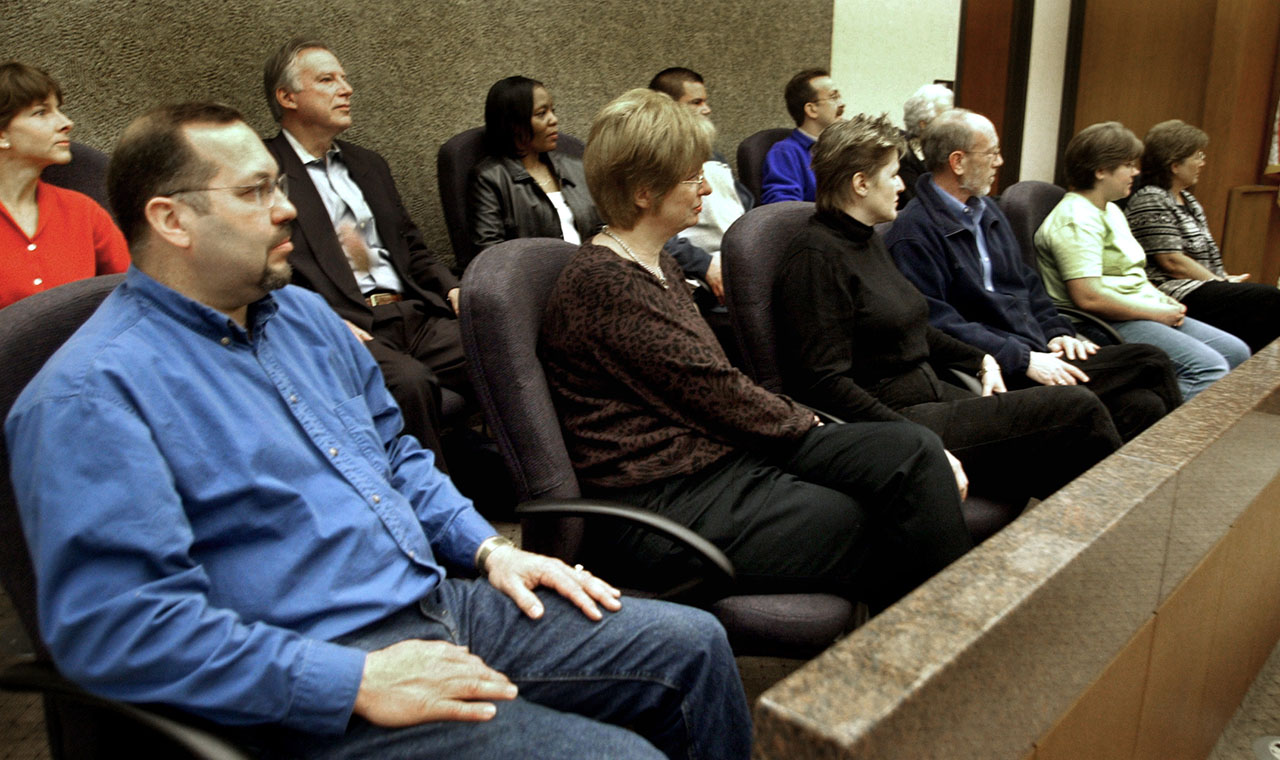A jury and other attendees sitting in rows of chairs at a hearing or meeting.