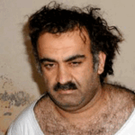 A man with dark hair and a mustache wearing a white Supreme Court t-shirt.