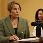 Massachusetts Governor Maura Healey speaking at a podium with a woman standing behind her.