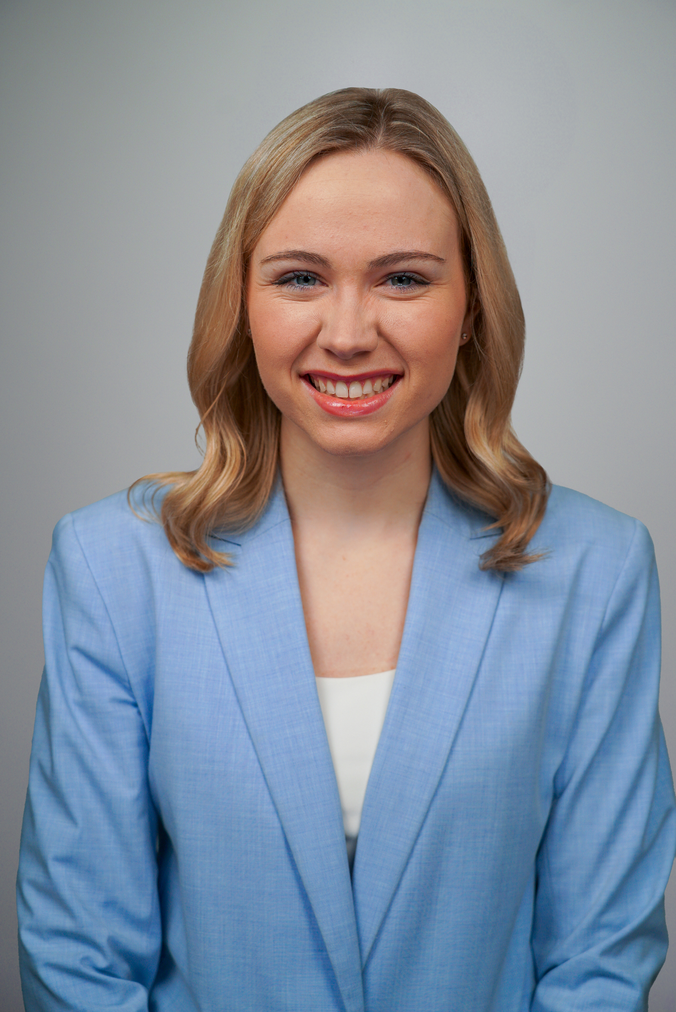A smiling woman with blonde hair, a Daily Signal intern, wearing a light blue blazer over a white shirt.