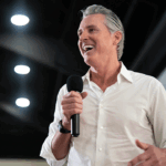 Gavin Newsom smiling and speaking into a microphone at a property.