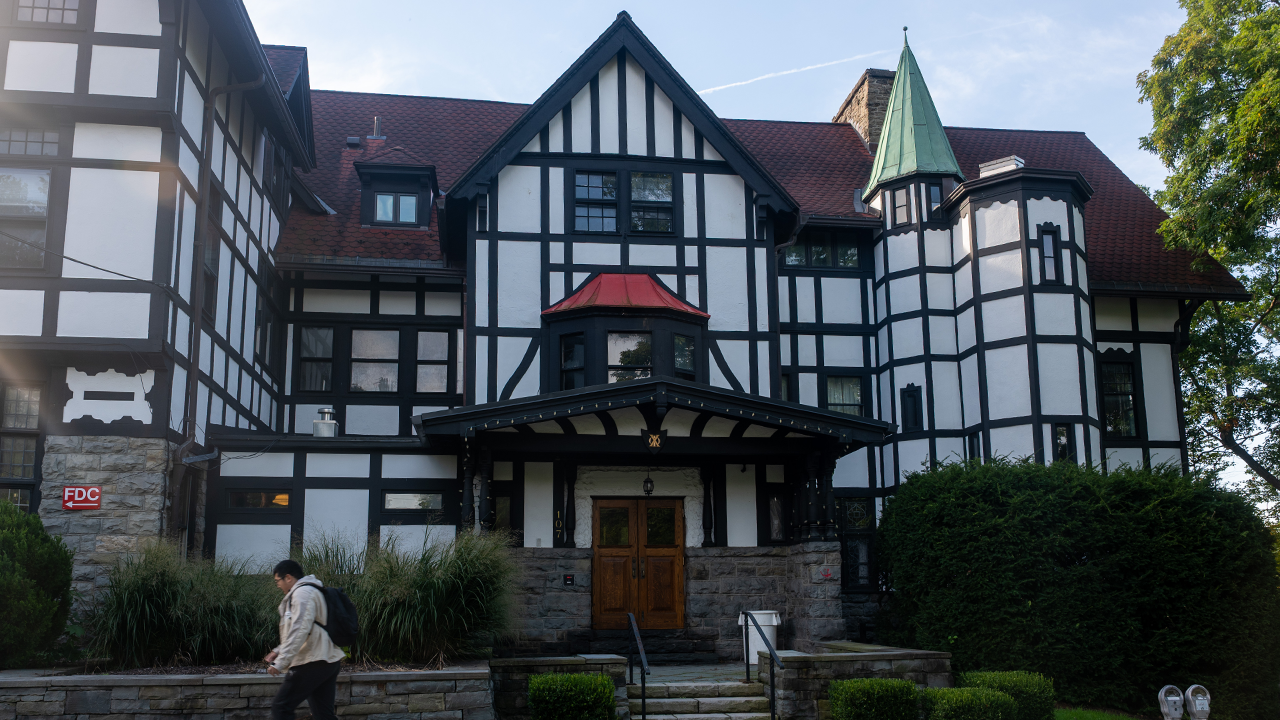 Home 1 A large Tudor-style building with white walls, dark timber framing, and a red roof, with a student walking past the entrance.