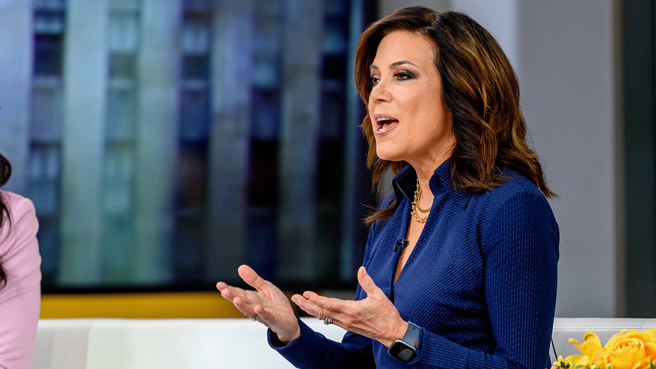 Home 2 Michelle Tafoya with shoulder-length brown hair wearing a dark blue pinstriped button-down shirt speaks while gesturing with her hands in a television studio.