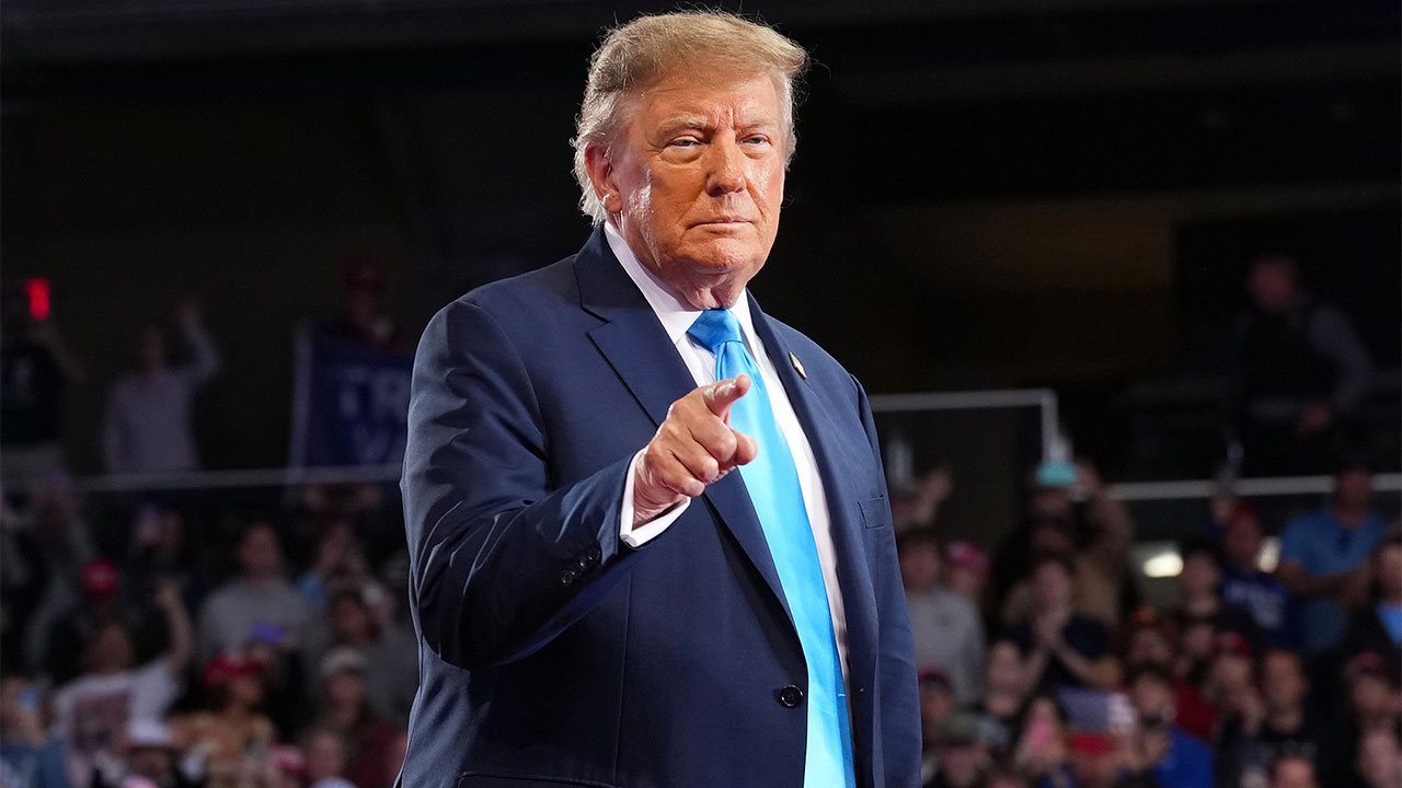 Home 1 Donald Trump in a navy blue suit and bright blue tie pointing toward the camera at a freedom rally.