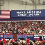 President Donald Trump speaks from a podium at a midterm campaign rally before a large crowd.