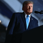 Donald Trump speaking at a podium in America with the Seal of the President of the United States.