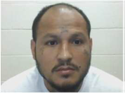 A man with a beard and receding hairline, wearing a white shirt, looks at the camera. The background is a white tiled wall.