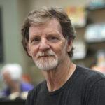 Masterpiece Cakeshop baker Jack Phillips, prosecuted by the Colorado Civil Rights Commission but vindicated by the Supreme Court. A middle-aged man with light brown hair, a beard, and mustache wears a dark t-shirt and sits indoors. Shelves with books and a chalkboard menu are blurred in the background.