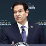 Marco Rubio, wearing a suit and patterned blue tie, speaks at a podium with a sign reading Ministerial on the Resurgence of Political Terrorism and a Department of State seal in front of a dark backdrop. He spoke about leftist terrorism.