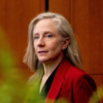 Virginia Gov. Abigail Spanberger supports the "Reproductive Freedom" amendment, which critics claim would invalidate laws against statutory rape. Pictured: Spanberger, with long gray hair, wearing a red blazer and black top, stands indoors in front of a wood-paneled background with green blurred leaves in the foreground.