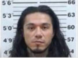 EXCLUSIVE: ICE Arrests 5 Criminal Illegal Aliens 5 A man with long dark hair and a short beard faces forward in front of a height chart, similar to a mugshot. The chart behind him displays measurements in feet and inches, and the setting suggests an ICE processing area.