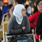 Conservatives can only effectively combat Islamism if we also defend Muslims' religious freedom. The Dallas airport foot washing controversy highlights this key distinction. Pictured: A woman in a white headscarf and gray sweater sits in a wheelchair in an airport, surrounded by people in line. The wheelchair has a DFW sign on it.