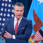 Secretary of War Pete Hegseth at a podium briefing reporters.