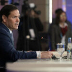 Side view of Marco Rubio sitting at a table and speaking.