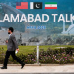 A man walks by a large sign reading "Islamabad Talks"