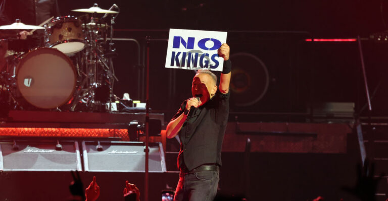 Bruce Springsteen, in concert, holding up a "No Kings" sign.
