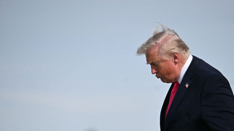 Donald Trump with his head down against a light blue sky.