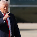 Donald Trump walking across the tarmac with Marine One in background pointing.