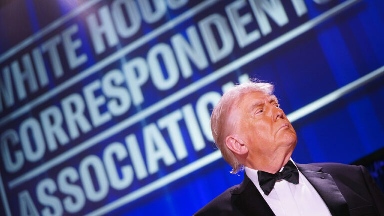 President Trump in profile in bottom right of shot underneath large "White House Correspondents' Dinner" sign.