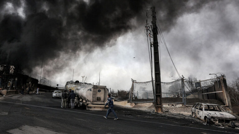 Dark smoke clouds engulf destroyed vehicles near an ongoing fire following an overnight airstrike on the Shahran oil refinery in northwestern Tehran.