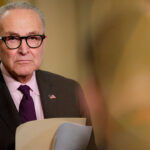 A dour-looking Chuck Schumer holding a file.