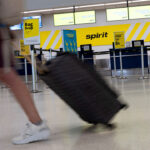 A woman drags her luggage past an empty Spirit Airlines counter at an airport.