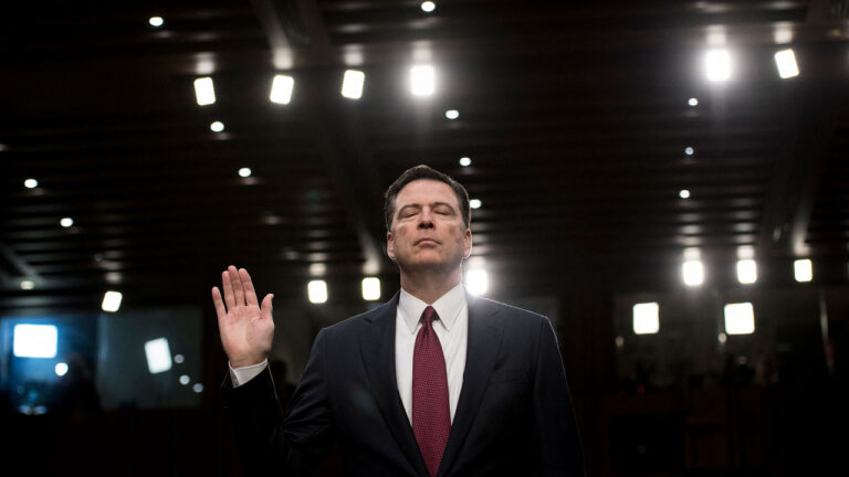 James Comey, with his eyes closed, raises right hand before giving congressional testimony.