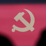 The communist emblem is seen framed by the silhouettes of two people during a press conference of the Central Committee of the Communist Party of China (CPC).