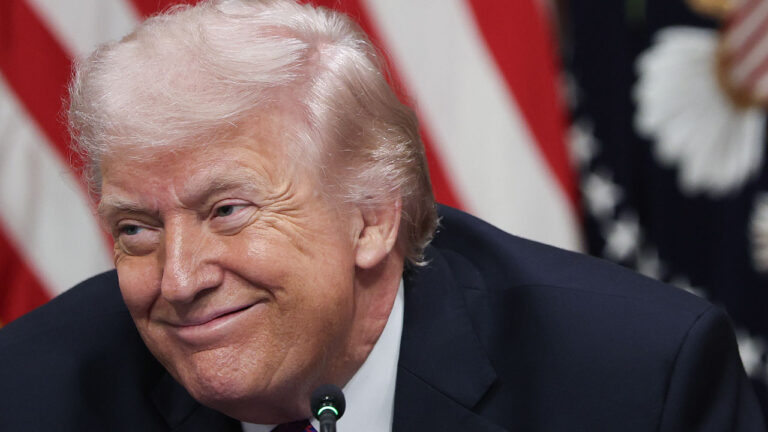 Close-up of Donald Trump grinning, with an American flag as a backdrop.