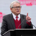 Ohio Gov. Mike DeWine points a finger upward while delivering a speech.