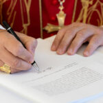 Close-up of hands of Pope Leo as he signs encyclical "Magnifica Humanitas."