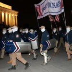 Members of the white nationalist group Patriot Front, wearing masks and carrying shields, gather at the Lincoln Memorial at night.