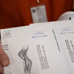 Close-up of mail-in ballots being held by a red-shirted worker.