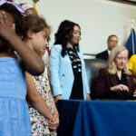 Virginia Gov. Abigail Spanberger signs a bill as an adorable little girl in a blue dress covers her eyes.