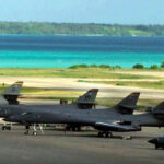 American fighter planes sit on a runway at Diego Garcia base with beautiful blue island waters in background.