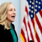 Abigail Spanberger with her mouth open, American flag in the background.
