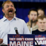 Graham Platner yells from behind a podium with supporters behind him.