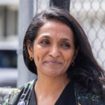 Nithya Raman standing against a chain link fence.