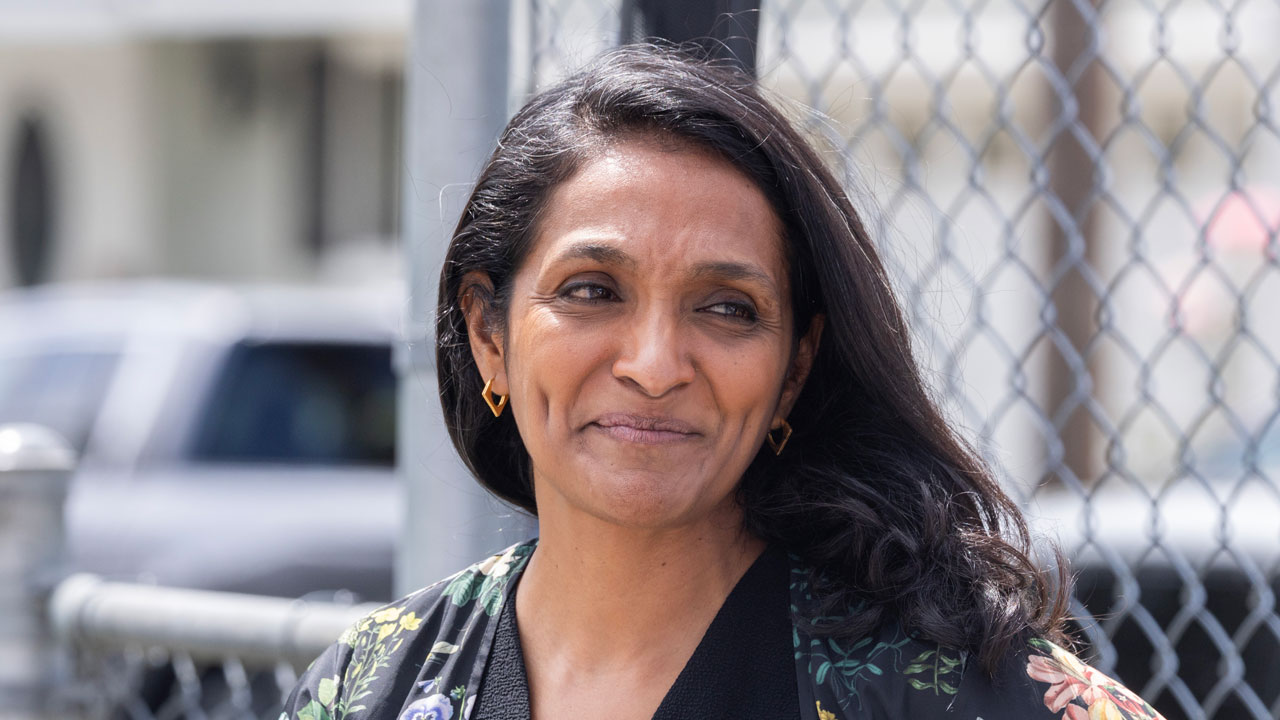 Nithya Raman standing against a chain link fence.