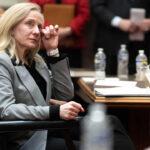 Abigail Spanberger, in a grey suit, wipes a tear from her eye while seated at a table.