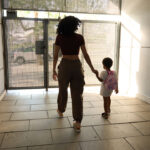 Young black woman leads child toward outside door.