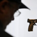 Silhouette of man looking at a display of a handgun against a white background.